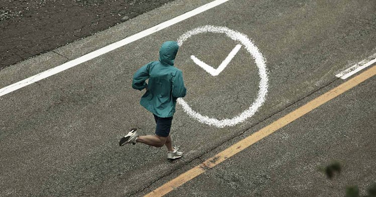 Someone runs on the street in a blue jacket on grey pavement