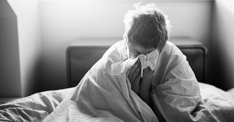 A sick kid wrapped in a blanket blows his nose