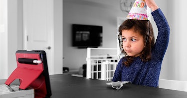 a girl in a birthday hat celebrates a birthday in front of a tablet
