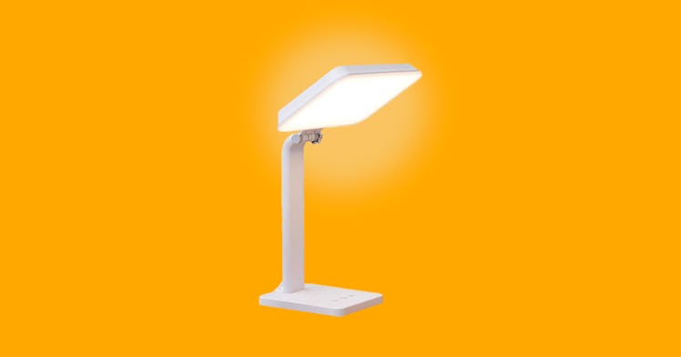 A white SAD lamp, a sun lamp for seasonal affective disorder, turned on and set against an orange ba...