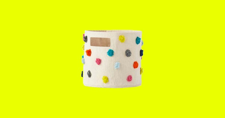 white canvas toy storage basket with multicolored pom poms isolated on neon yellow background