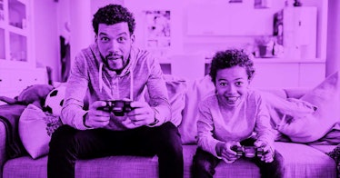 A dad and son sitting on the couch in their living room playing video games together - purple color ...