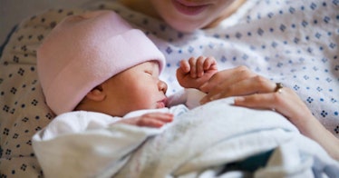 mother in hospital gown holding swaddled newborn baby girl