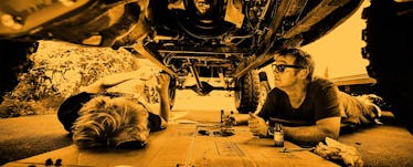 A dad and his son under a car looking at the different parts of the car and fixing it