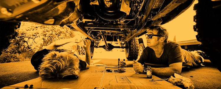 A dad and his son under a car looking at the different parts of the car and fixing it