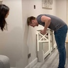 A man attempts the chair challenge at home while his wife looks on.