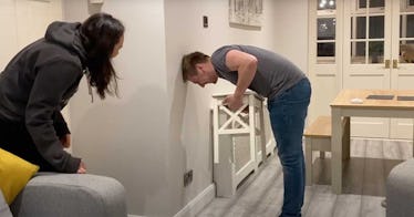 A man attempts the chair challenge at home while his wife looks on.