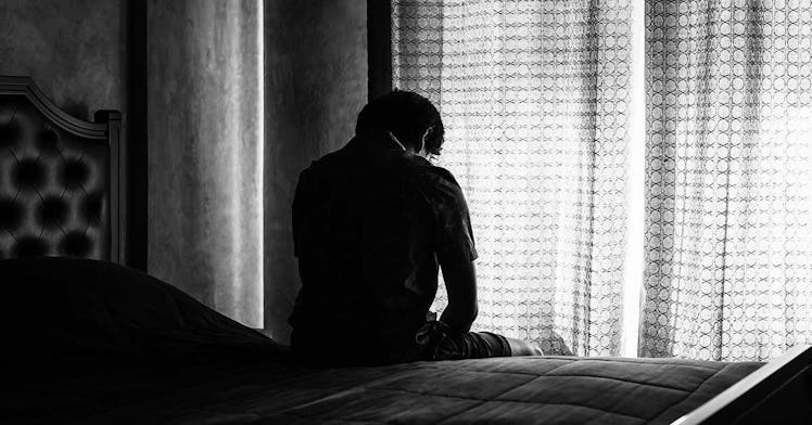 man experiencing divorce tried, sits on bed and sadly looks out a window