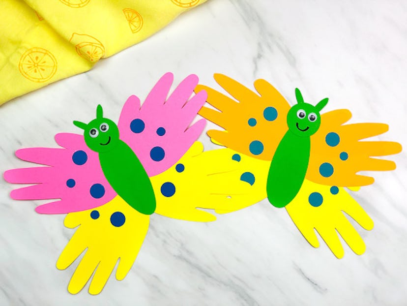 two construction paper butterfly crafts in pink, yellow, and orange laying flat on a marble counter