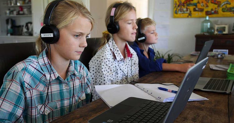 Three white children sit on computers with headphones on