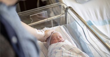 A newborn in an incubator being touched on the head by the hand of an adult, depicting historic baby...