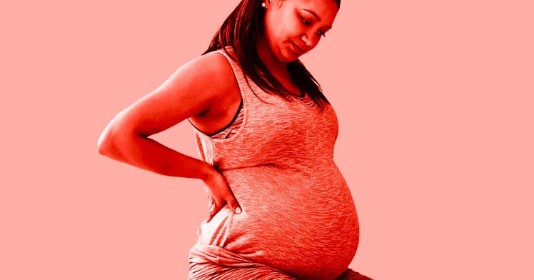 a pregnant woman experiencing bleeding during pregnancy rests her right hand on her waist as she loo...