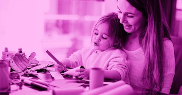 pink photo edit of a young girl working on construction paper crafts while sitting in her mother's l...