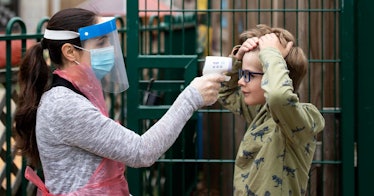 A kid receives a temperature check by an adult in full PPE
