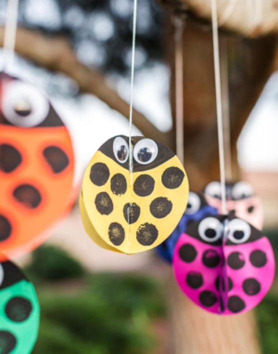 colorful construction paper ladybugs with black polka dots and googly eyes, hanging from a tree