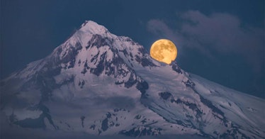 A moon rises over a snowy mountainous peak at night