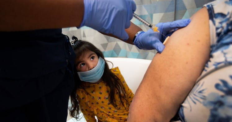 A masked child watches an adult get vaccinated