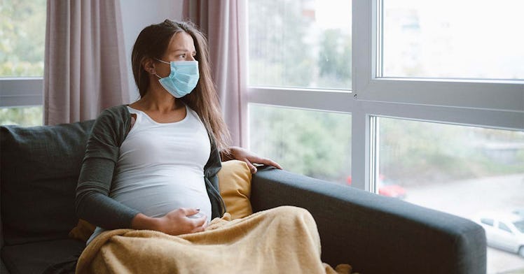 A pregnant woman in a mask has a yellow blanket on her lap