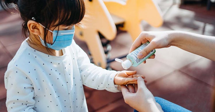 A toddler wearing a mask gets hand sanitizer squirted on their hand