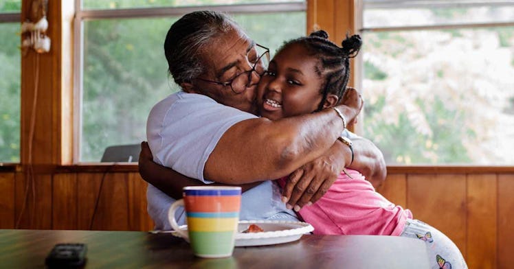 woman in white shirt sitting at kitchen table hugging her granddaughter following CDC guidelines