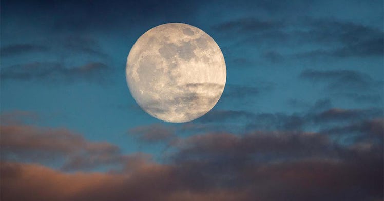 A white pale moon over a dark blue sky with pink clouds
