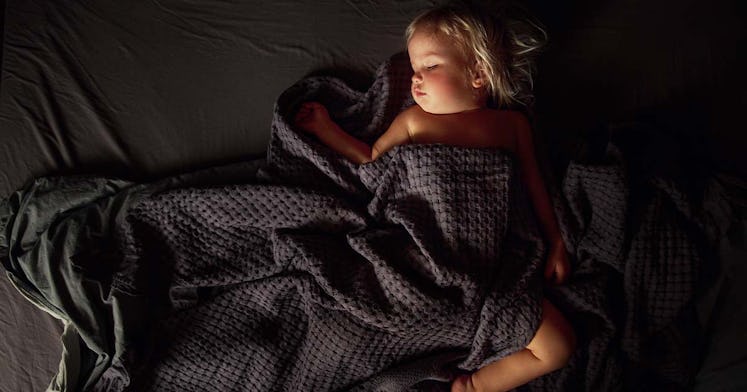 a sleeping toddler under a dark blanket in a montessori bed made up with dark sheets