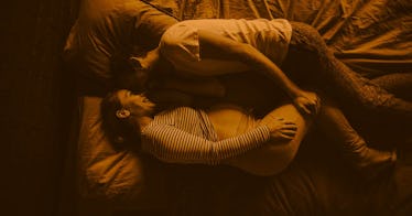a pregnant woman lays in bed with her partner as they prepare for a perineal massage
