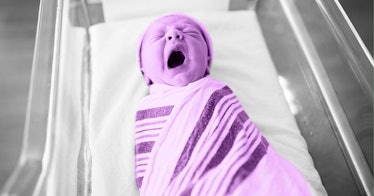 A swaddled baby with a cap yawning in a hospital bassinet