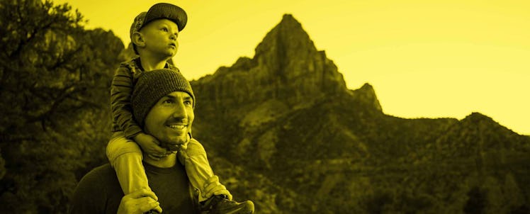 man with son on shoulders hiking through mountains