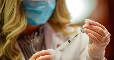 A blonde woman wearing a blue mask holds a syringe