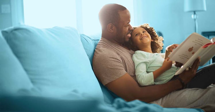 A father sitting on a blue couch with his daughter in his lap, reading her a book of poems