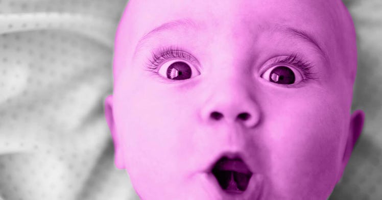 A baby with their mouth open in a coo and their eyes wide