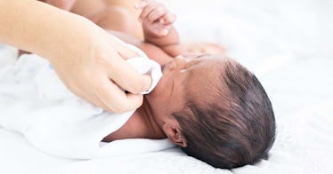 color photo of a mother wiping a newborn's cheek with a cloth -- not from a baby wipe warmer