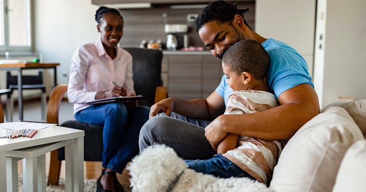 A black father sits with his child and smile while the mother looks at them, also smiling