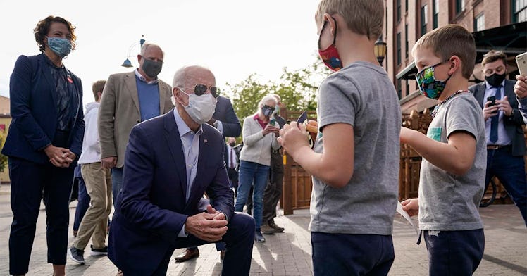 Biden, on his knee, talks to children, all wearing masks