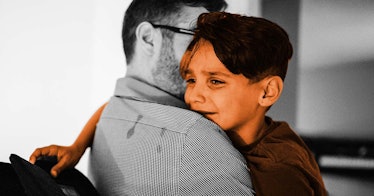 A boy who's crying rests his head on the shoulder of a man who is comforting him, depicting a scenar...
