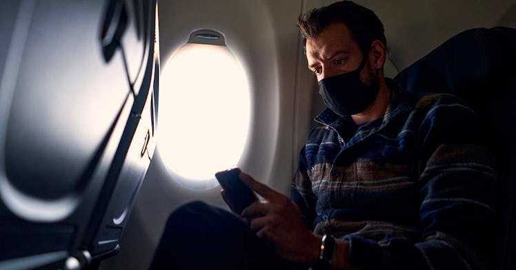 A person sits on a plane wearing a mask