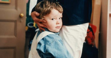 A child who appears to be shy clings to a parent's pant leg