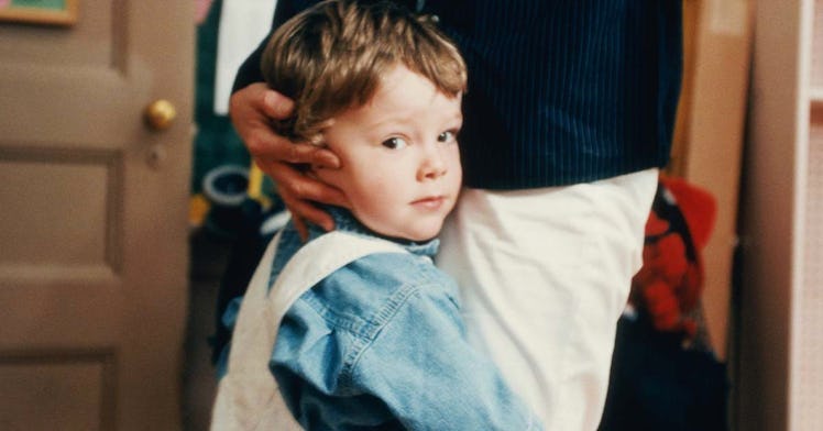 A child who appears to be shy clings to a parent's pant leg