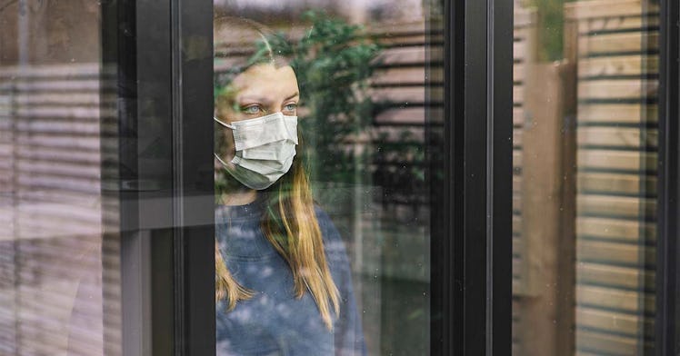 A person wears a mask and stares out of a window