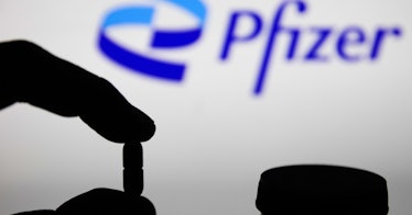 A hand holds a pill in front of a Pfizer logo