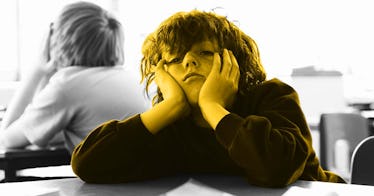 A child looking bored holding his head in his hands and leaning on a desk