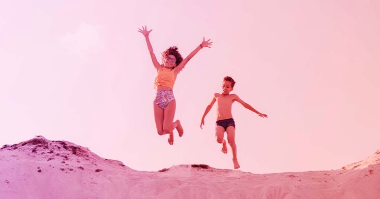 A boy and girl run along the beach together with the girl jumping in the air