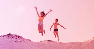 A boy and girl run along the beach together with the girl jumping in the air