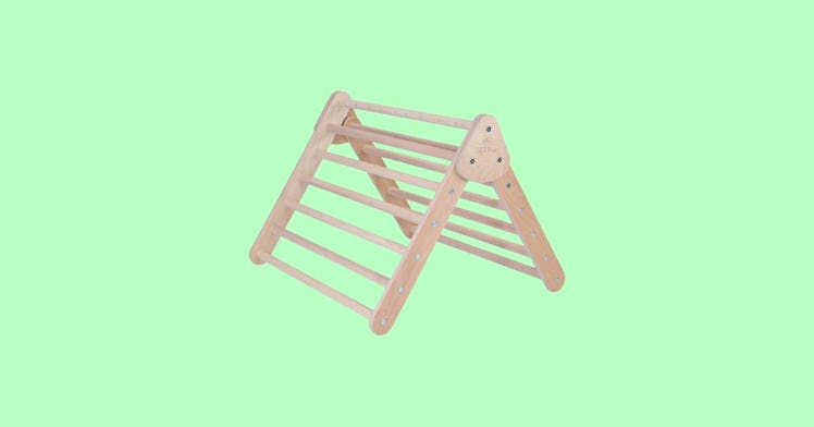 A pikler triangle, aka a toddler climbing wall, against a green backdrop
