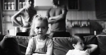 Parents arguing with one another in the background while children sit stoically on the couch.