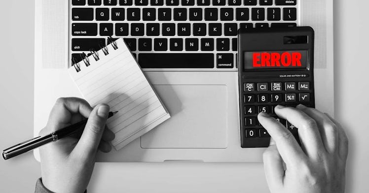 A man calculates taxes on a laptop with a calculator and notepad