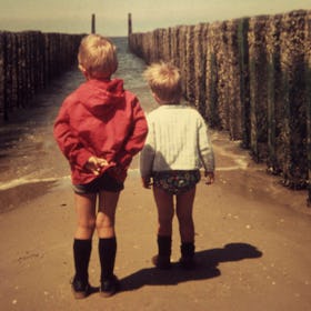 Sepiatone photo of two children in 1980s style clothing looking out to sea