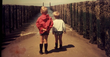 Sepiatone photo of two children in 1980s style clothing looking out to sea