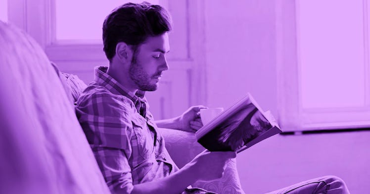 A man in a plaid shirt sitting on a sofa reading a book with a purple color filter